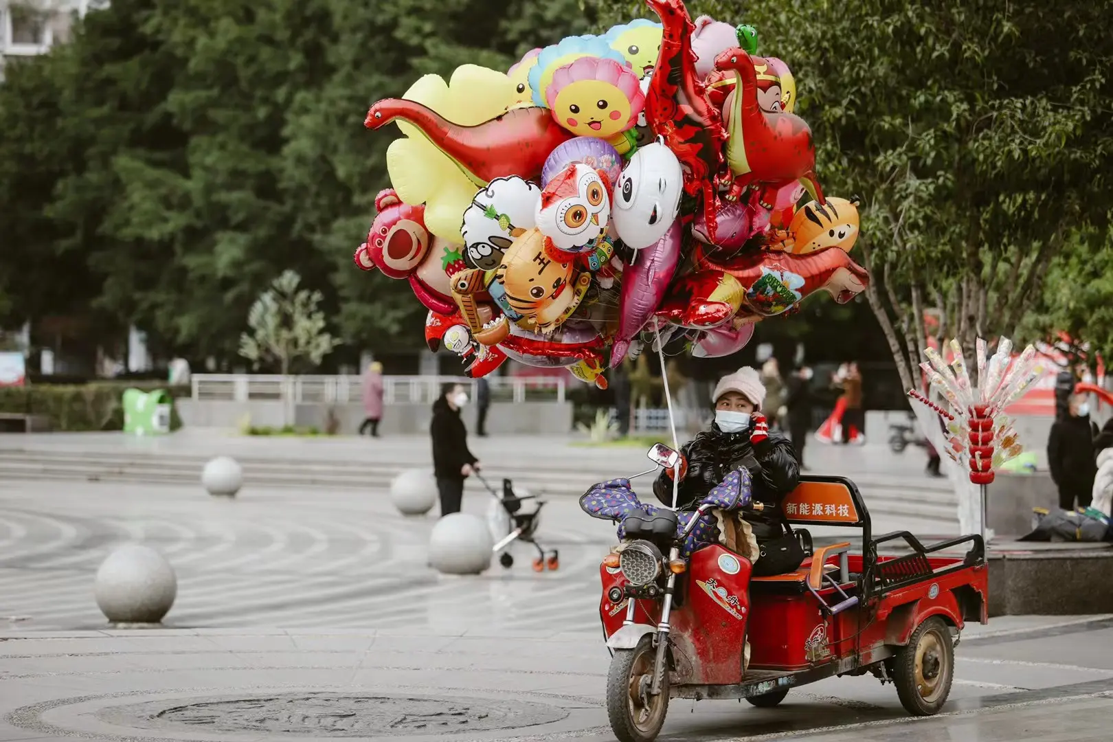 A street vendor riding beneath a colorful cluster of balloons