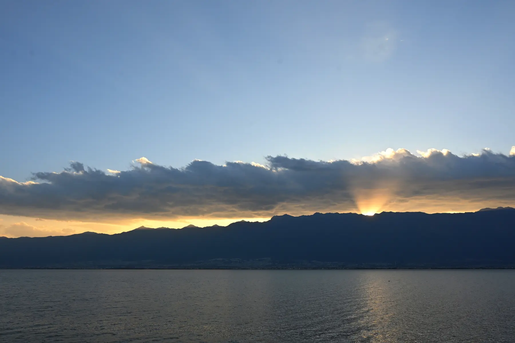 Sunset breaking through clouds above mountains and a lake in Dali