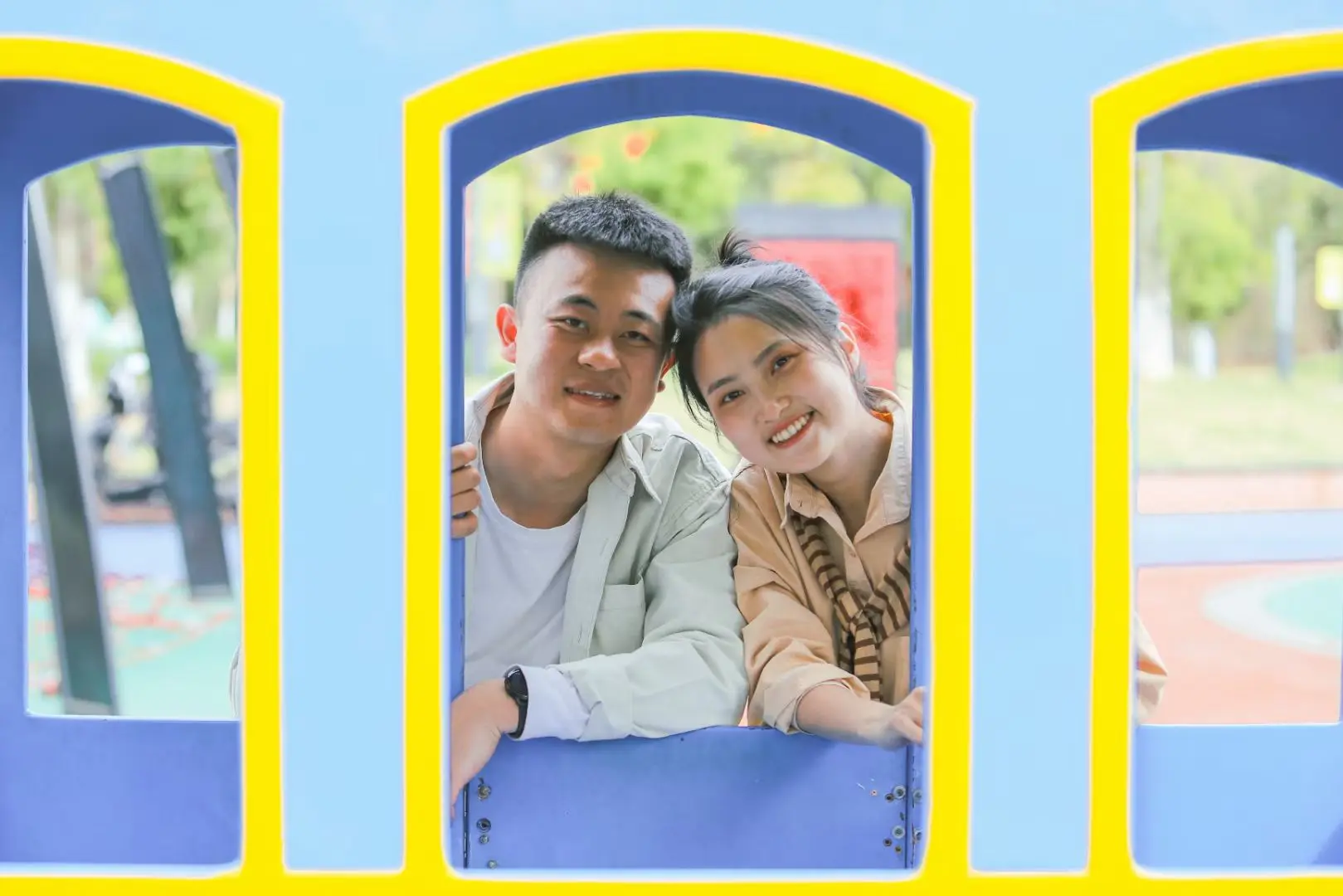 A smiling couple framed by a colorful playground window