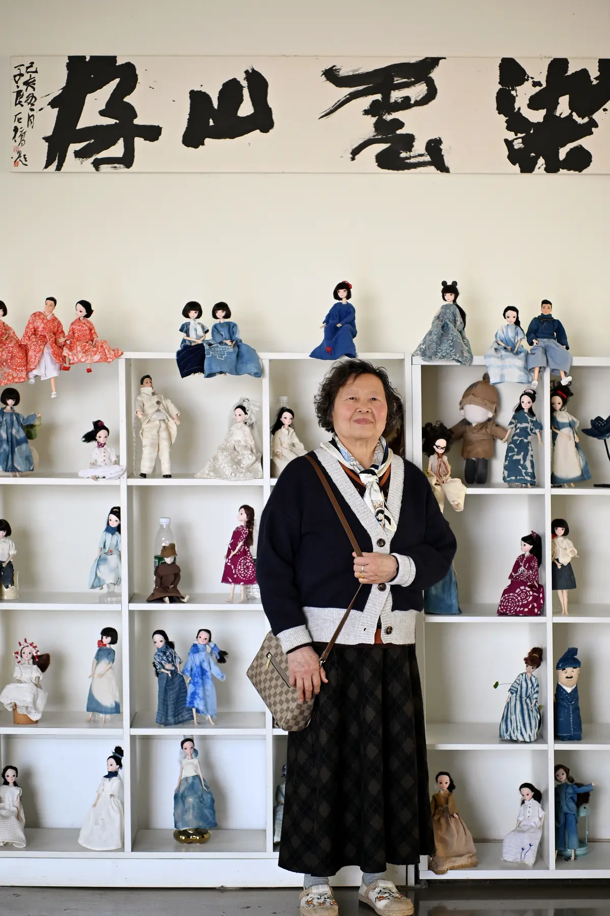 An older craft artist standing among handmade dolls